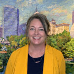 Portrait of Susan Tate, Festival of the Arts Director, in front of a painting of the downtown skyline in the Arts Council of Oklahoma City offices.