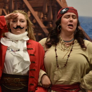 Two opera singers dressed as pirates pose on stage for kids at a summer library concert.
