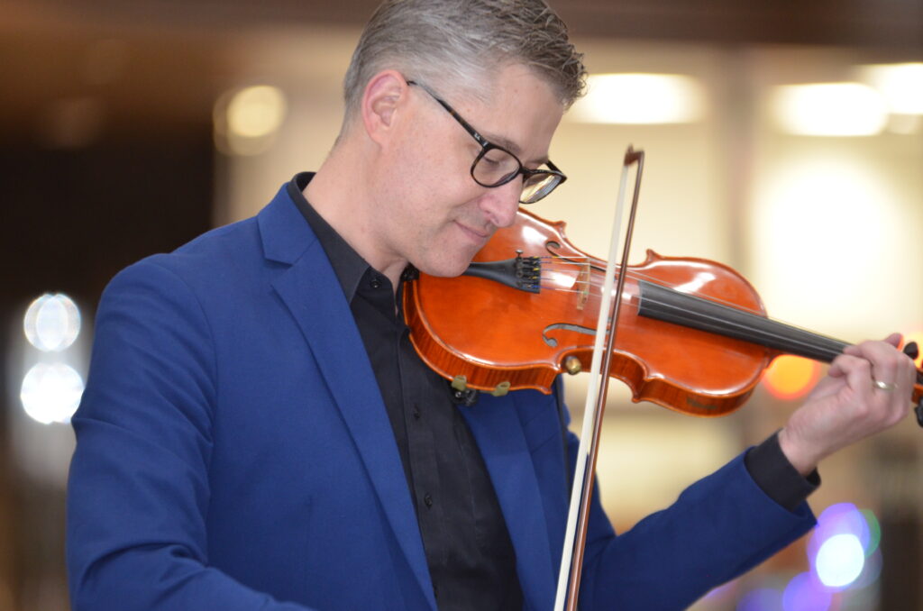 Profile of a man in a blue suit playing the violin.