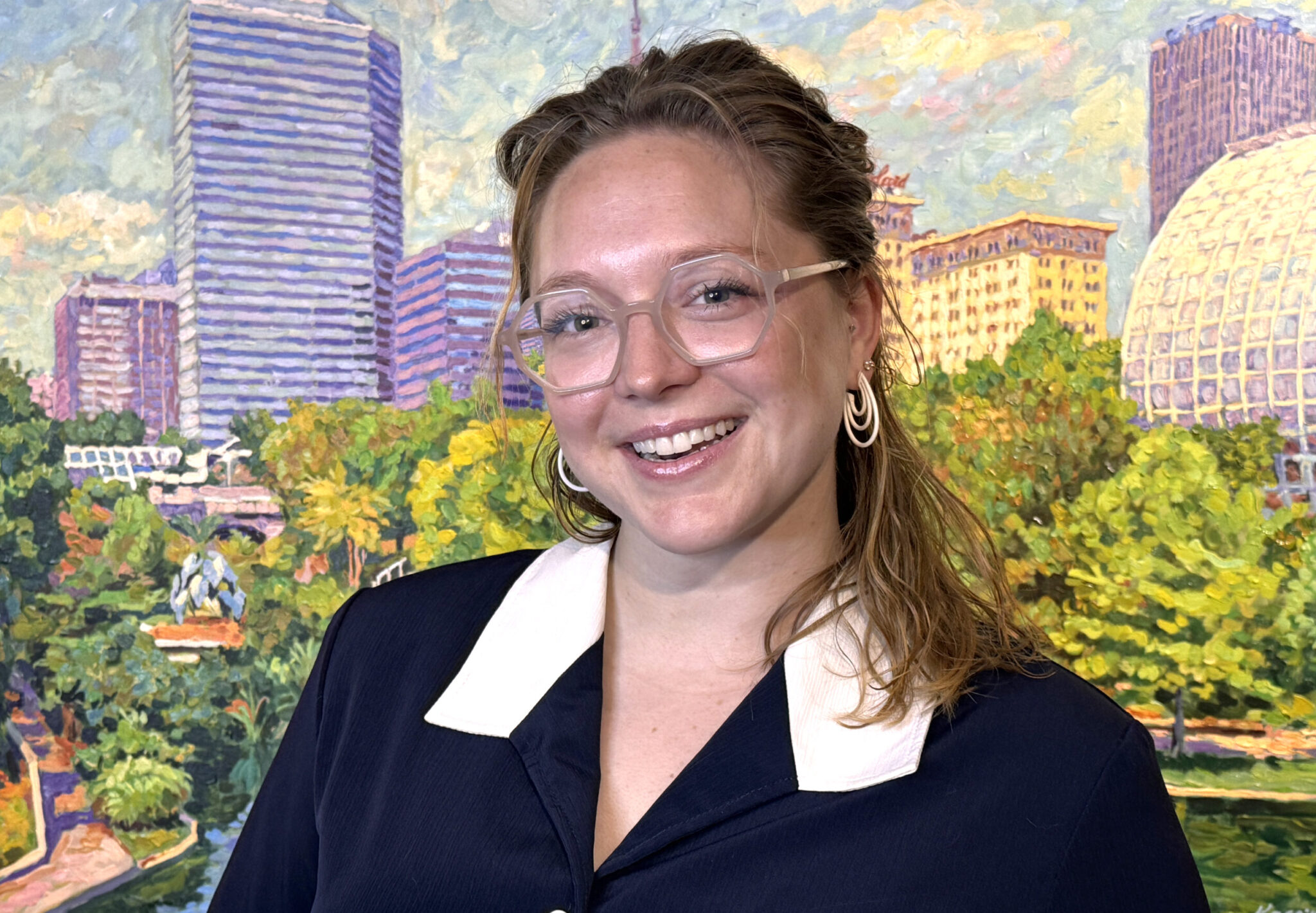 Woman standing in front of a painting of the OKC skyline.